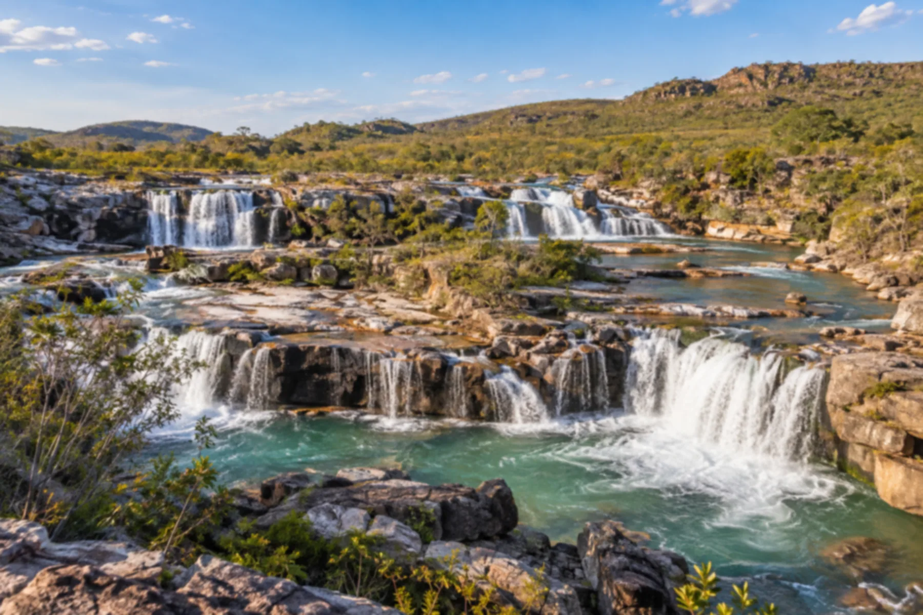 Sequência de quedas d'água largas sobre lajes de rocha clara em paisagem aberta de cerrado.