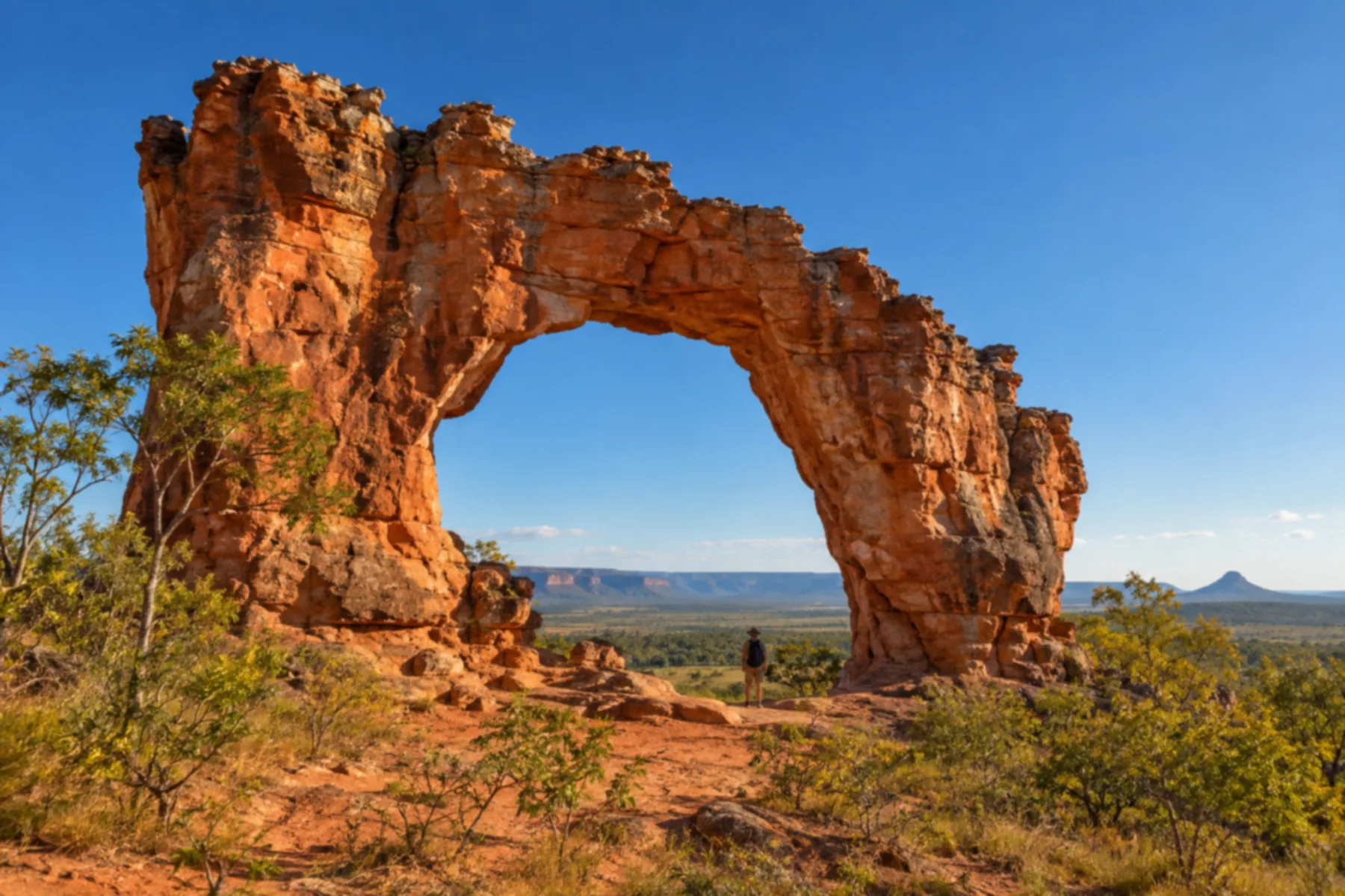 Grande arco natural de rocha avermelhada isolado no cerrado.