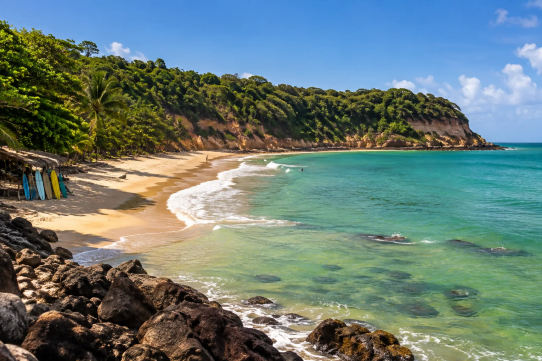 Praia em curva com mar verde-esmeralda calmo.