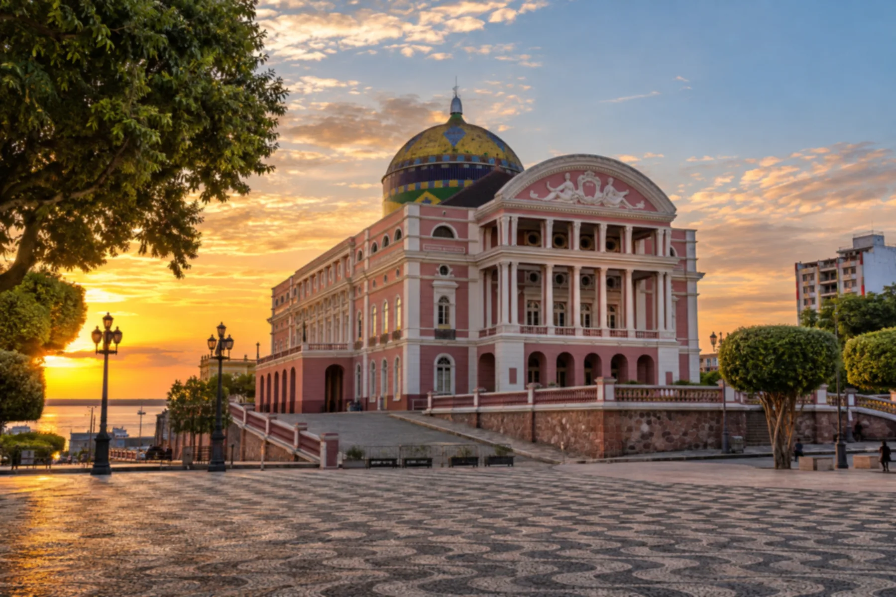 Fachada rosada e cúpula colorida do Teatro Amazonas ao entardecer.