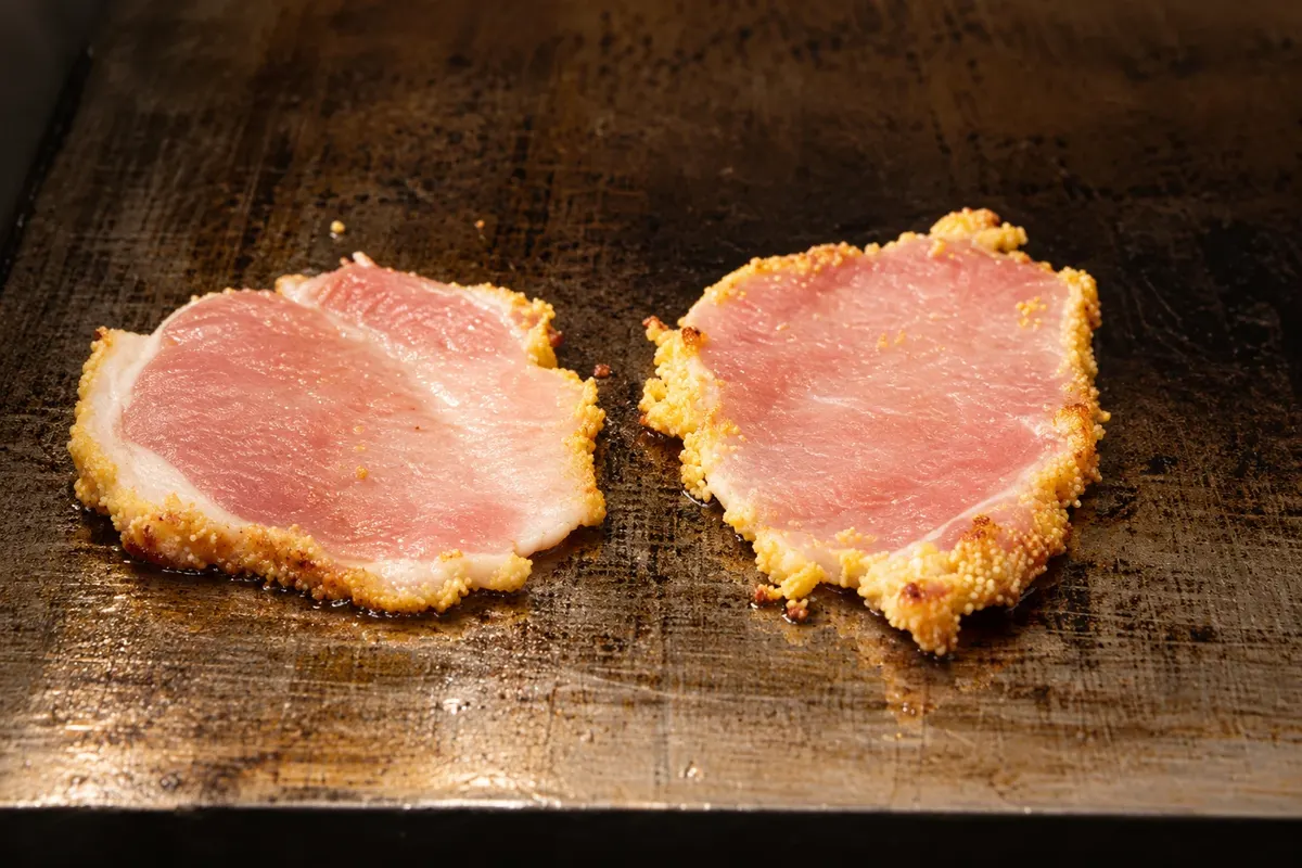 Detalhe de fatias de peameal bacon com crosta de fubá na chapa.